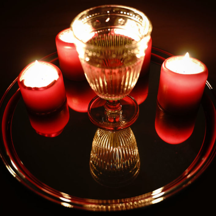 Kerzen und ein Weinglas spiegeln sich auf einem Tablett